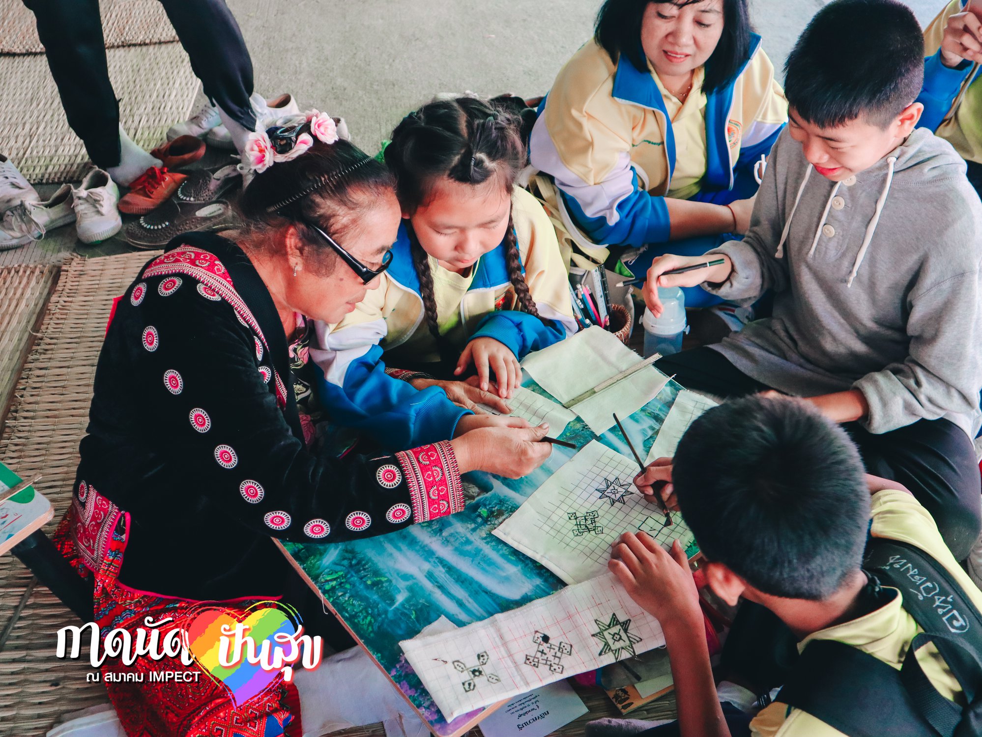 A woman sits at a table with children to teach them Hmong patterns